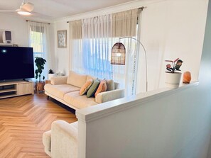 Una sala de estar con sofá, televisión, planta y lámpara colgante.