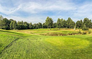 En golfbana med välskött gräs, träd och en klar himmel.