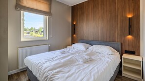 Ein Schlafzimmer mit Bett, Fenster mit Blick, Heizkörper und einer Holzwand.
