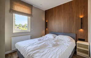 Ein Schlafzimmer mit Bett, Fenster mit Blick, Heizkörper und einer Holzwand.