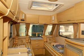 Interior compacto de autocaravana con dos camas, una kitchenette y una ventana pequeña.