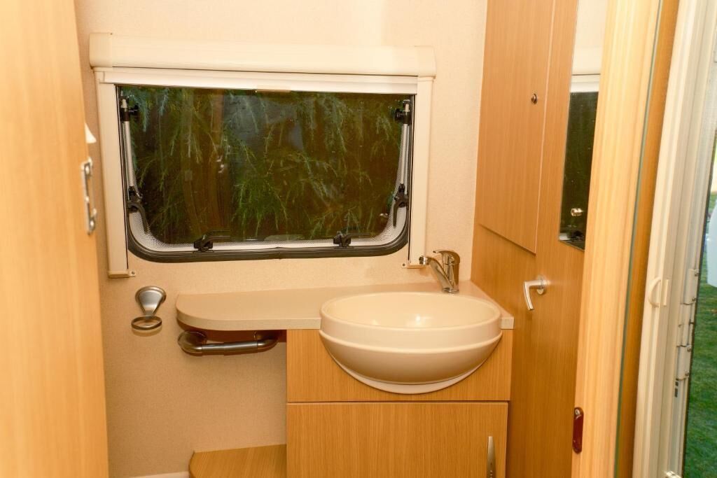 Un baño pequeño con ventana, lavamanos y armarios de madera.