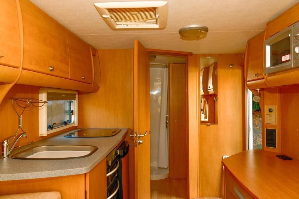 Cocina compacta con lavamanos, estufa y microondas, y zona de ducha visible a través de una puerta abierta.