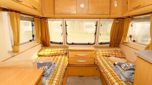 A compact RV interior with two beds, a small table, and a cabinet.