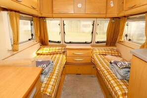 A compact RV interior with two beds, a small table, and a cabinet. - Sundale Caravan Retreat 2 Berth - Wanaka (Wānaka)
