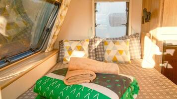A compact RV bedroom with a bed, pillows, a window, and a small table.