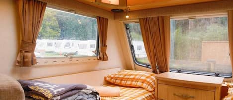 Ein kompaktes Wohnmobil-Interieur mit einem Bett, einer kleinen Kommode und zwei Fenstern.