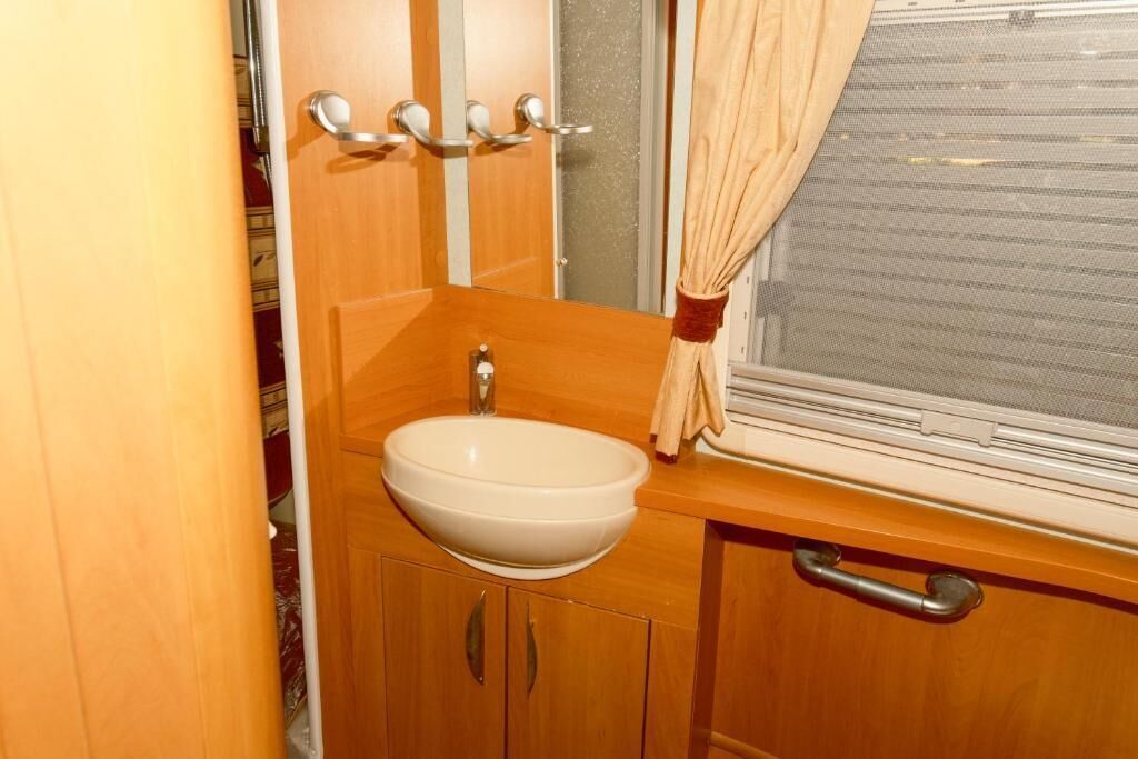 Un baño pequeño con lavamanos, armarios de madera y una ventana con cortina.