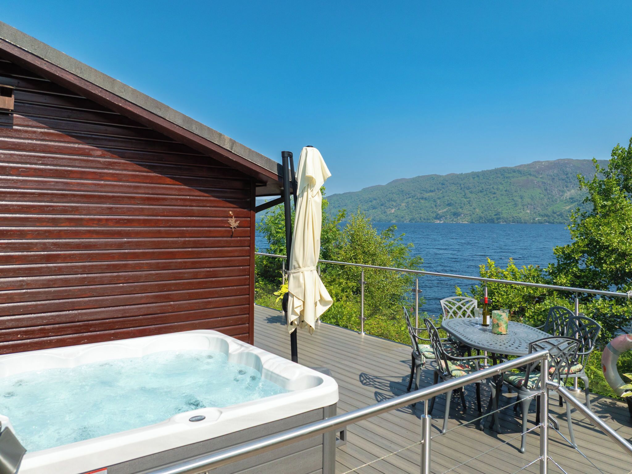 A hot tub on a wooden deck with a view of a lake and hills.