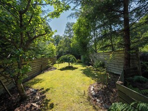 Ein Garten mit Holzzaun, einem kleinen Baum und einer Rasenfläche.