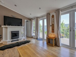 Ein modernes Wohnzimmer mit Kamin, Flachbildfernseher und Blick ins Freie.