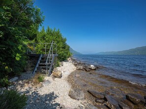 Eine felsige Küstenlinie mit einer Metalltreppe, die zum Wasser hinabführt, umgeben von dichtem Grünwerk.