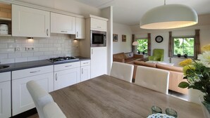 A modern kitchen with white cabinets, a built-in microwave, and a dining area with a wooden table and chairs. - 3 bedroom stunning home in Den Ham (Den Ham)