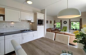 A modern kitchen with white cabinets, a built-in microwave, and a dining area with a wooden table and chairs. - 3 bedroom stunning home in Den Ham (Den Ham)