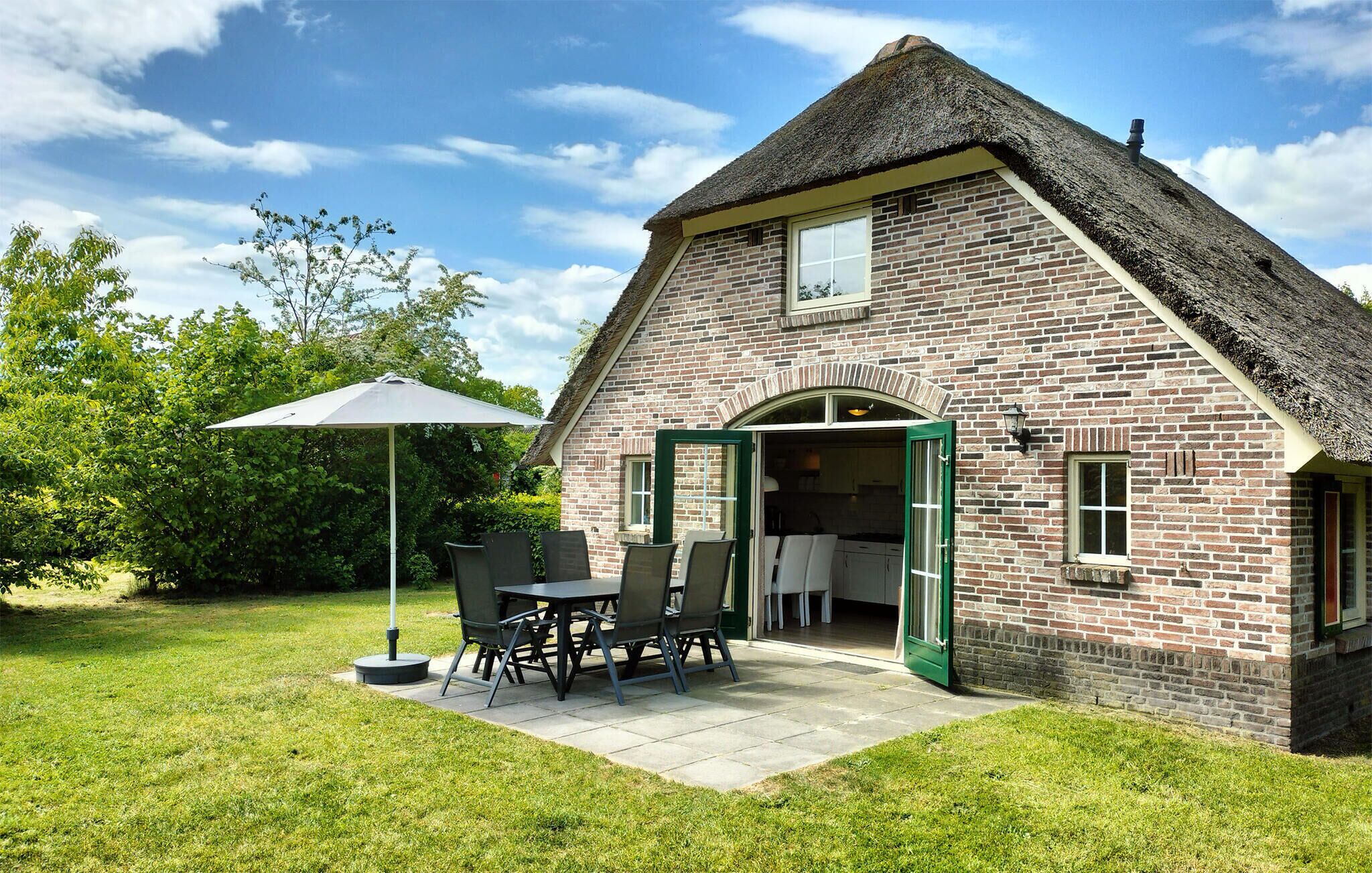 A brick house with a thatched roof, an open door, and a patio with a table and chairs.