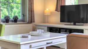 A room with a TV, a lamp, a table with a tray, and two potted plants by a window. - 3 bedroom stunning home in Den Ham (Den Ham)