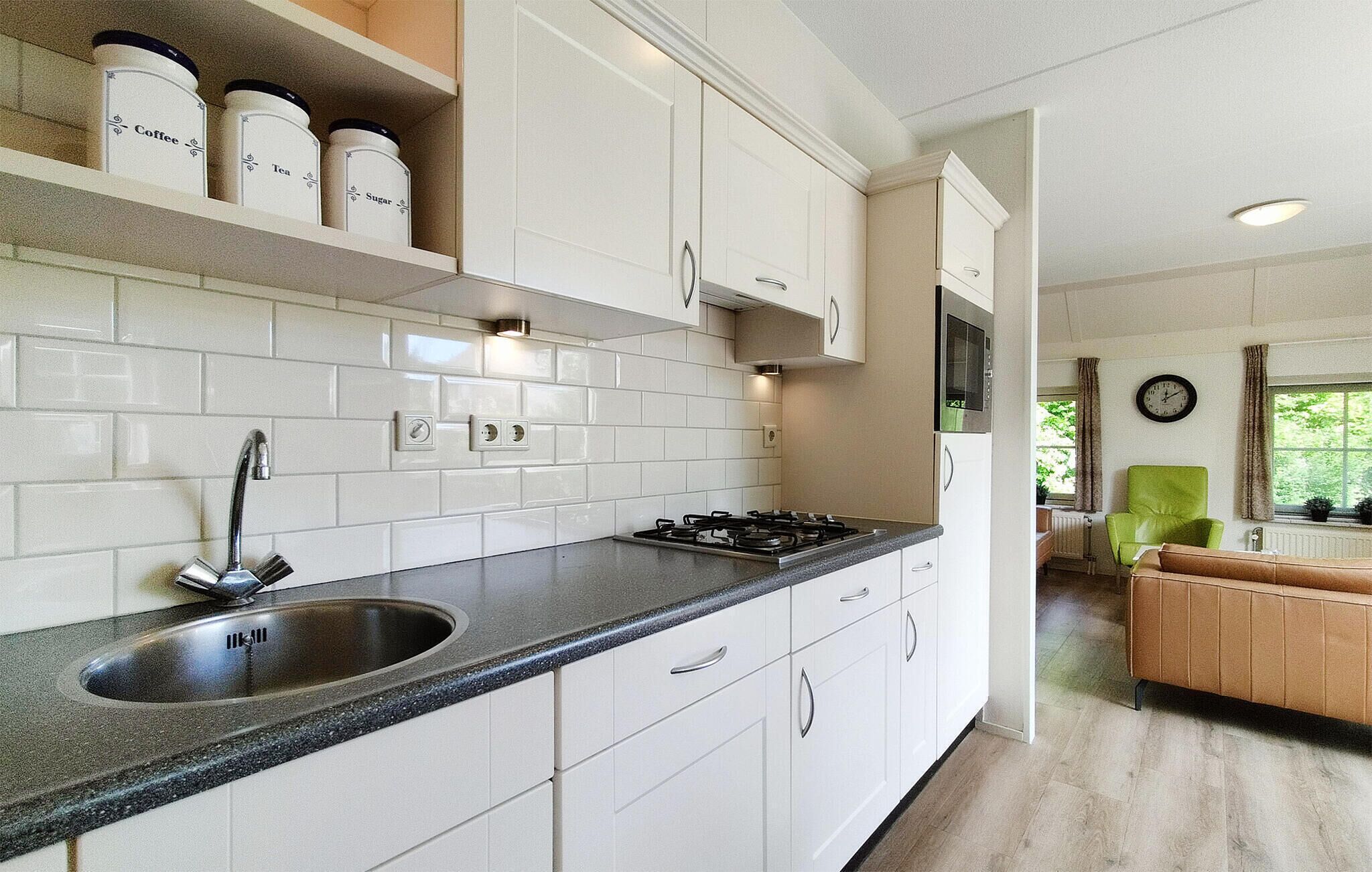 A kitchen with white cabinets, a stainless steel sink, and a gas stove. There are jars on a shelf labeled 'Coffee,' 'Tea,' and 'Sugar.'