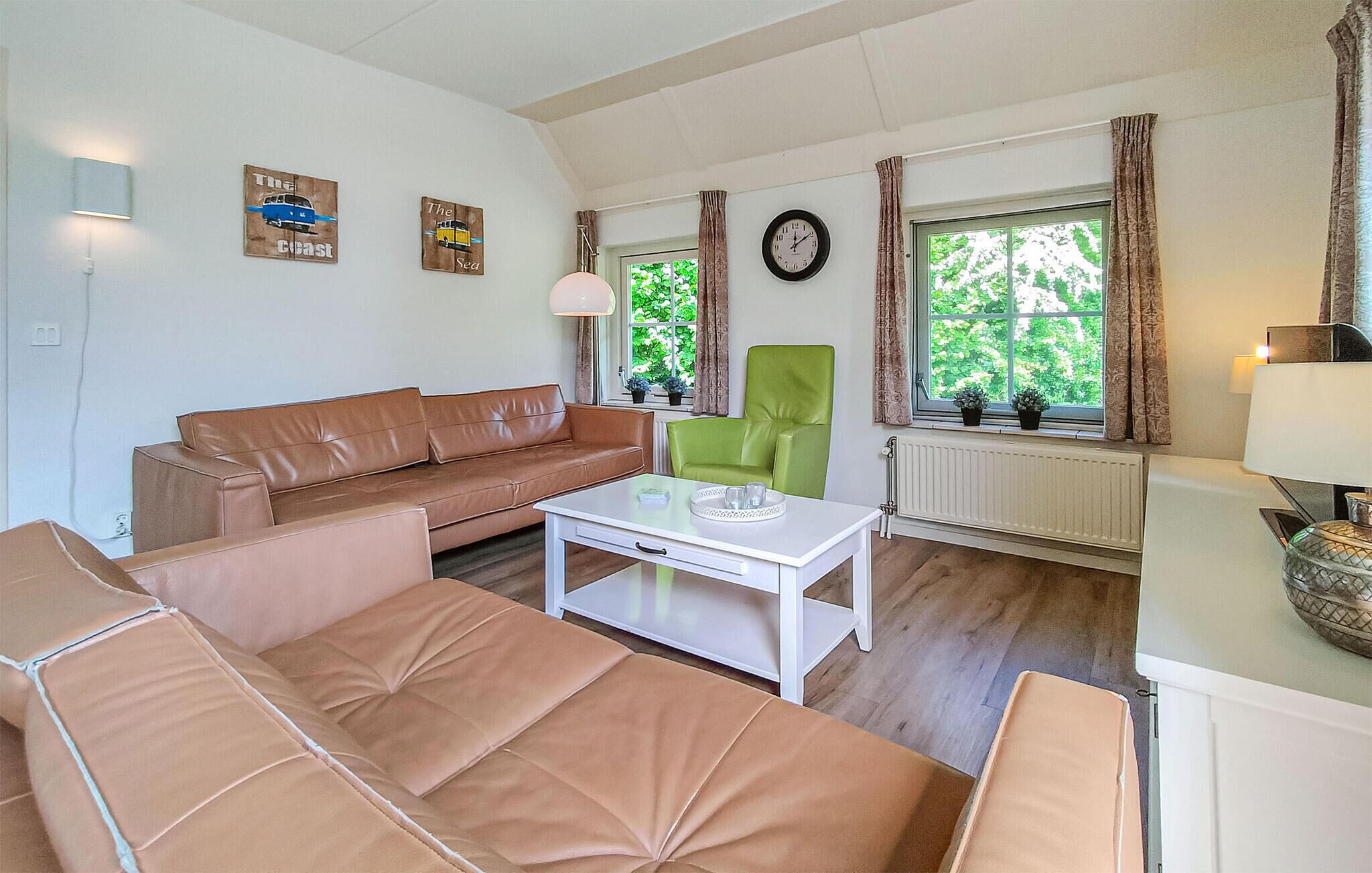 Ein Wohnzimmer mit braunem Ledersofa, einem grünen Sessel, einem weißen Couchtisch und einer Uhr an der Wand.