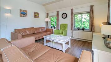 Ein Wohnzimmer mit braunem Ledersofa, einem grünen Sessel, einem weißen Couchtisch und einer Uhr an der Wand.