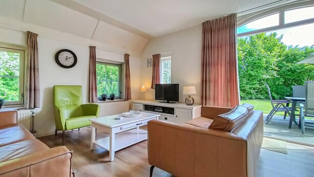 A living room with a sofa, a green chair, a coffee table, a television, and a window with curtains. - 3 bedroom stunning home in Den Ham (Den Ham)