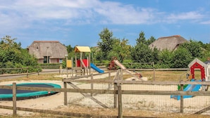 A playground with slides and a small pool, surrounded by a wooden fence and thatched-roof buildings. - 3 bedroom stunning home in Den Ham (Den Ham)