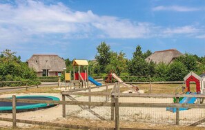 A playground with slides and a small pool, surrounded by a wooden fence and thatched-roof buildings. - 3 bedroom stunning home in Den Ham (Den Ham)
