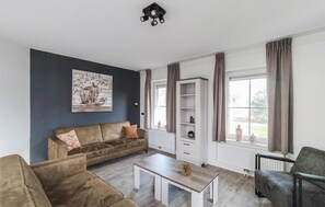 Ein Wohnzimmer mit einem braunen Sofa, einem weißen Couchtisch, einem Bücherregal und einem Fenster mit Vorhängen.