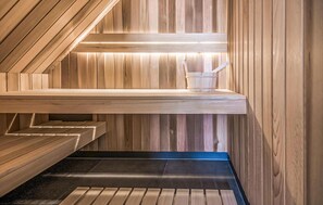Un sauna aux murs et aux bancs en bois, un banc avec un seau, et un plafond incliné.