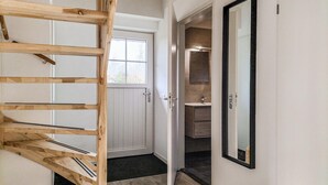 Puinen portaikko, joka johtaa valkoisiin oviin, kylpyhuone, jossa on peili ja pesuallas, sekä näkymä ulos ikkunasta.