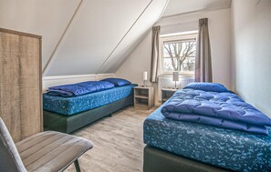 Ein kleiner, gemütlicher Raum mit zwei Betten, einem Sessel und einem Fenster mit Vorhängen.