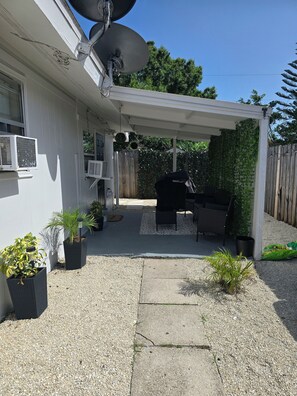 Un patio couvert comprenant un barbecue, du mobilier d’extérieur et des plantes en pot.