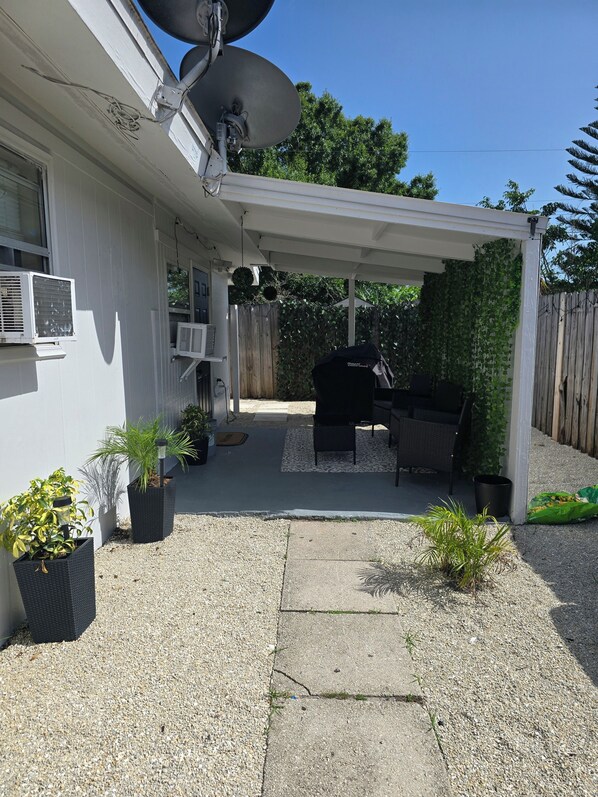 A covered patio area with a grill, outdoor furniture, and potted plants. - Cozy 1-bedroom studio in charming Sarasota. (Sarasota)