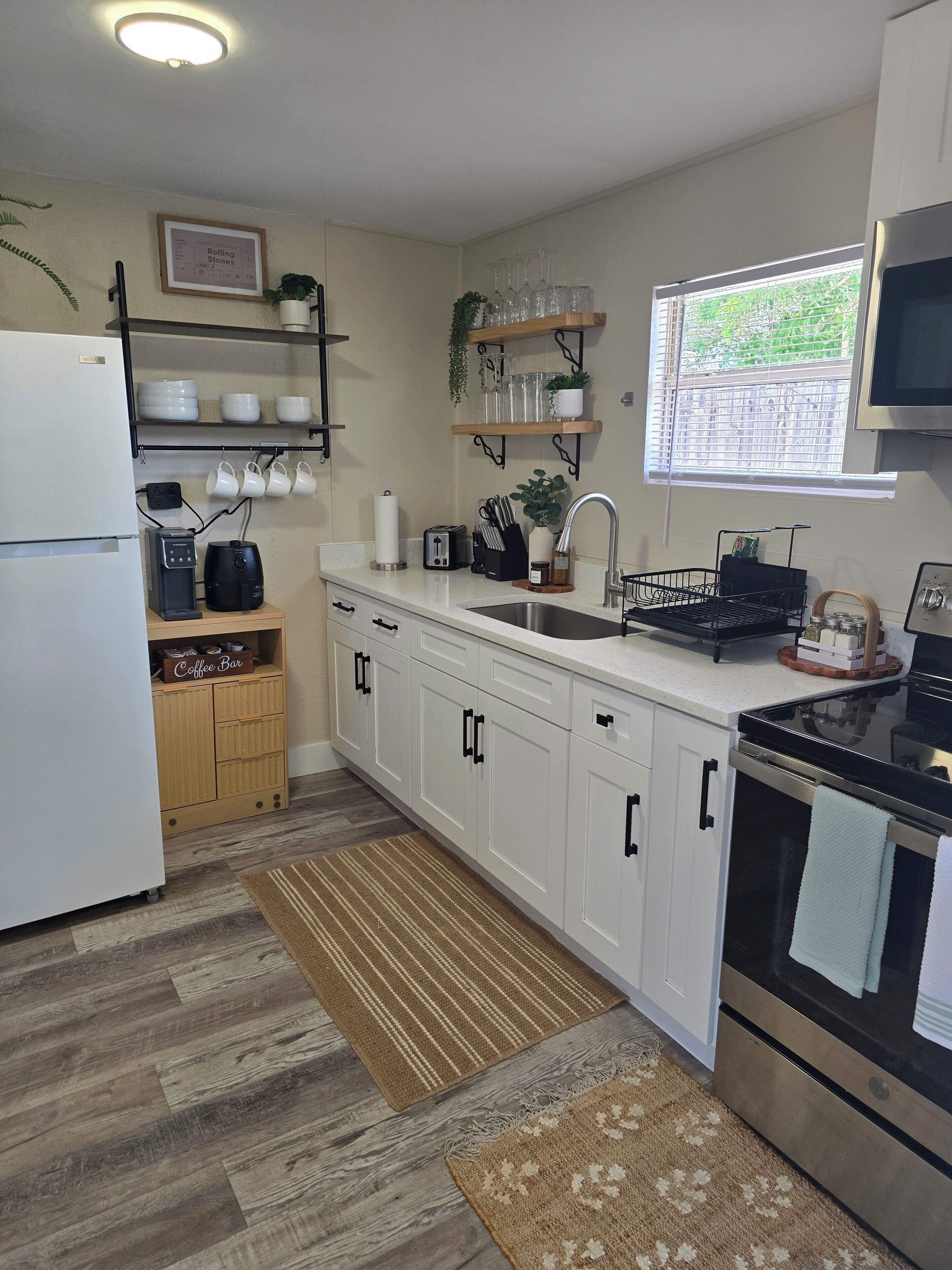 A modern kitchen with white cabinets, a stainless steel refrigerator, a coffee machine, and a microwave.