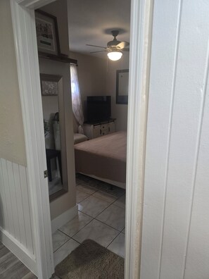 A bedroom with a bed, a ceiling fan, a TV, and a door leading to another room. - Cozy 1-bedroom studio in charming Sarasota. (Sarasota)