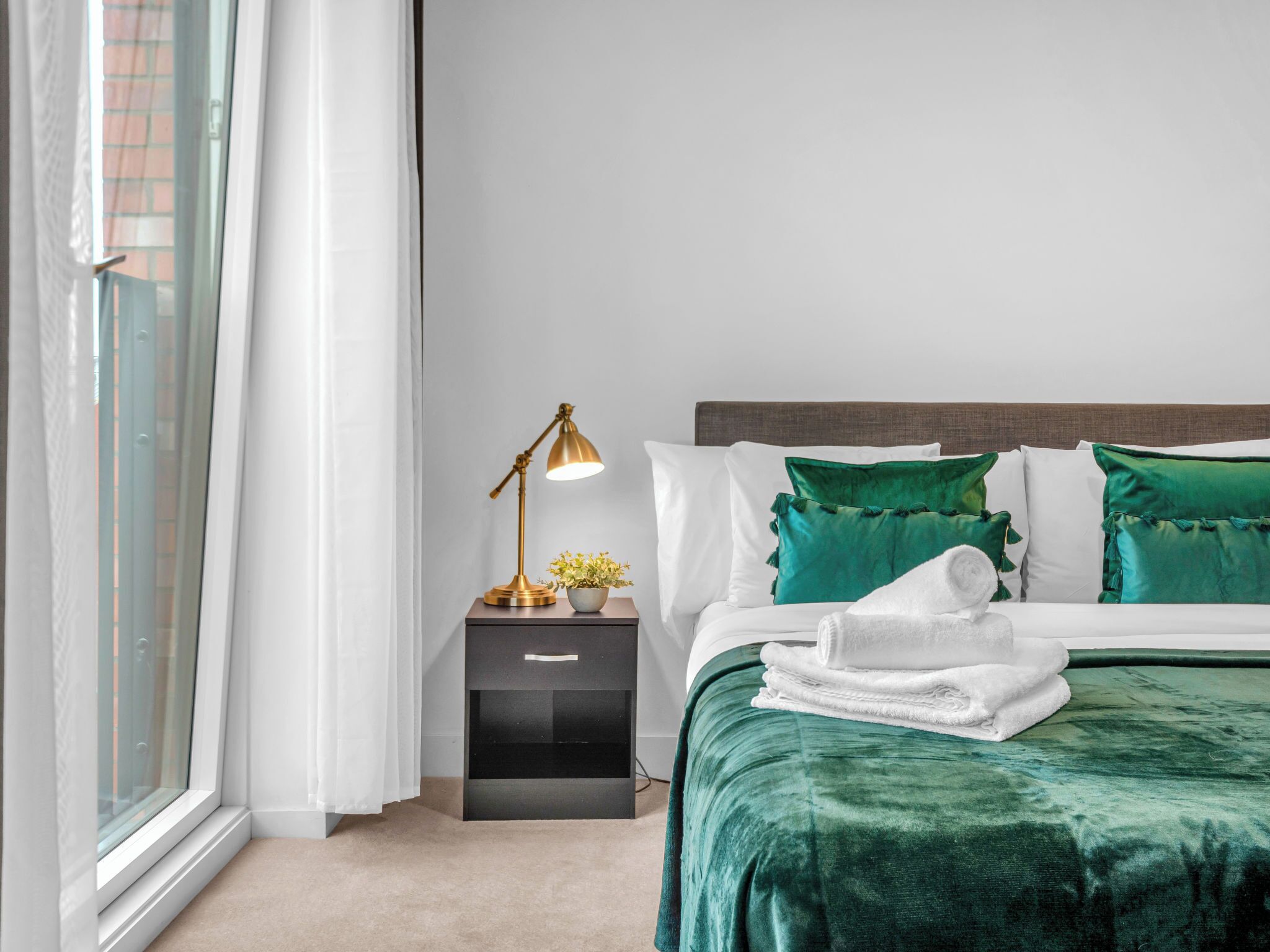 Una habitación de hotel con cama, mesita de noche, lámpara y ventana con cortinas.