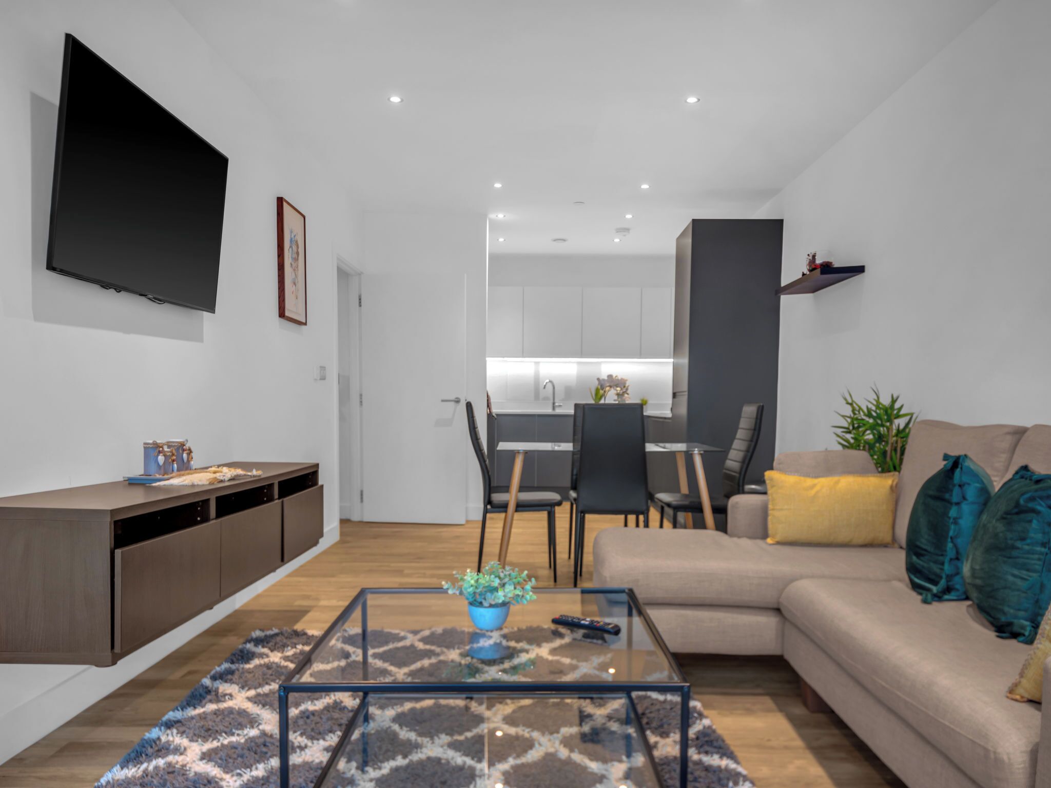 Una sala de estar moderna con un sofá, una mesa de centro y un televisor. Se ve una cocina al fondo.