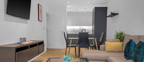 Una sala de estar moderna con un sofá, una mesa de centro y un televisor. Se ve una cocina al fondo.