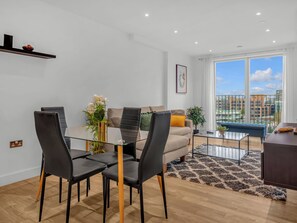 Ein modernes Wohnzimmer mit einem Glastisch, schwarzen Stühlen, einer Couch und einem großen Fenster mit Blick auf die Stadt.