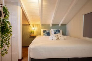 A hotel room with a bed, a nightstand with a lamp, a potted plant, and a view of the outside. - Spacious 3-bedroom condo in serene Jan Thiel with AC (Jan Thiel)