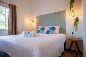 Ein ordentlich bezogenes Bett mit weißen Leinentüchern und blattgemusterten blauen Kissen, eine Nachttischlampe und ein kleiner Holzhocker.