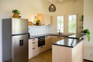 Une cuisine moderne dotée d’un réfrigérateur en acier inoxydable, de meubles en bois, d’un four encastré et d’un grand îlot central avec un plan de travail noir.
