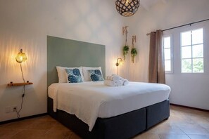 Ein Schlafzimmer mit einem Bett, Nachttischlampen, einer Wandpflanze und einem Fenster mit Vorhängen.
