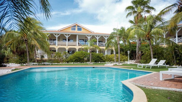 Una piscina de borde curvo, rodeada de palmeras y un edificio con balcones.