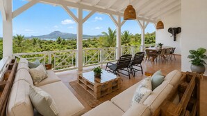 Un balcón amplio con vistas a un paisaje montañoso, amueblado con un sofá, sillas y una mesa de comedor.