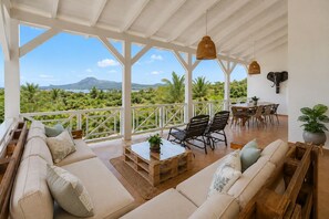 Ein geräumiger Balkon mit Blick auf eine gebirgige Landschaft, ausgestattet mit einer Couch, Stühlen und einem Esstisch.