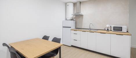 Cocina compacta con una mesa de madera, dos sillas, microondas, hervidor y horno empotrado.