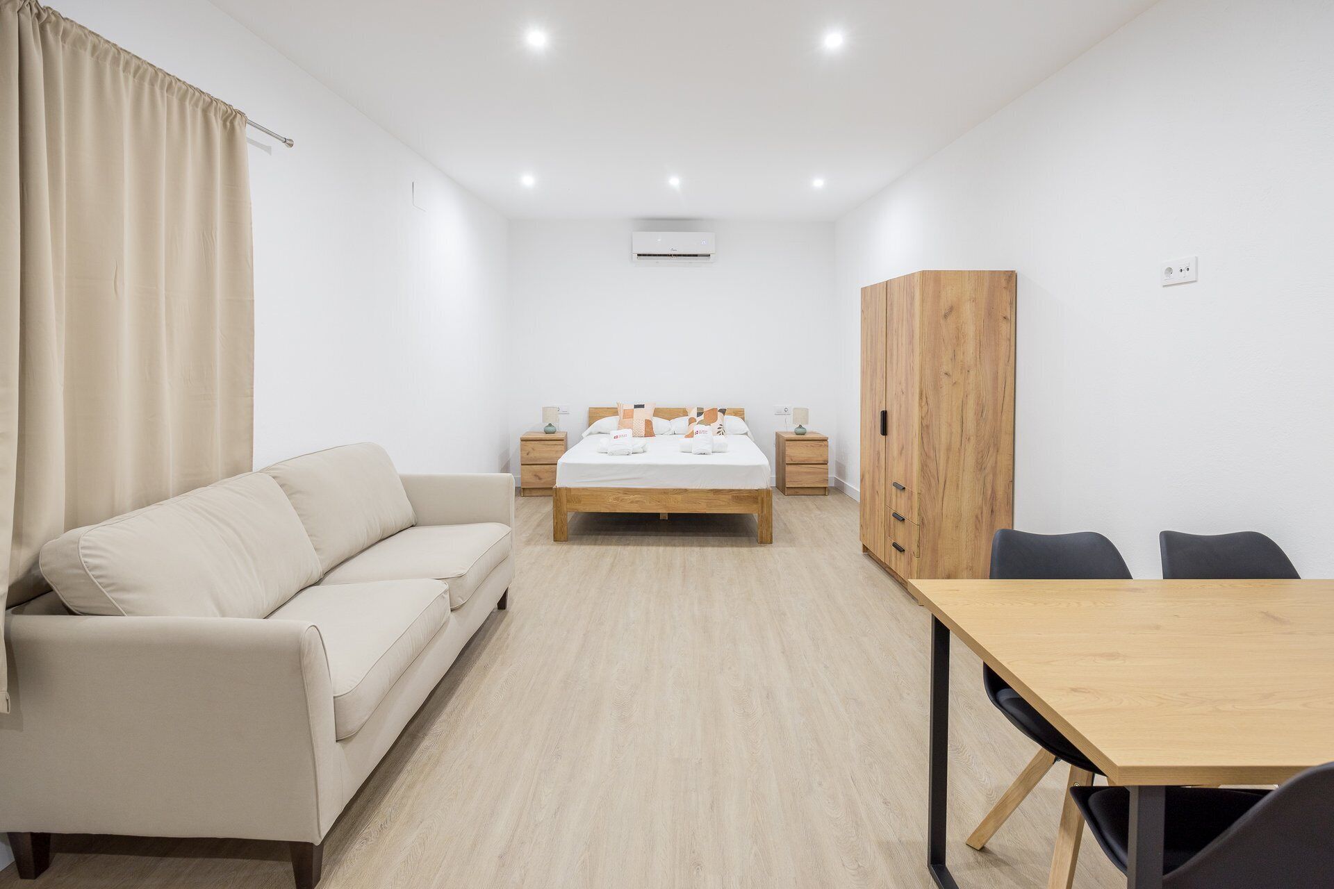A modern bedroom with a bed, a sofa, a wooden wardrobe, a desk, and a chair.