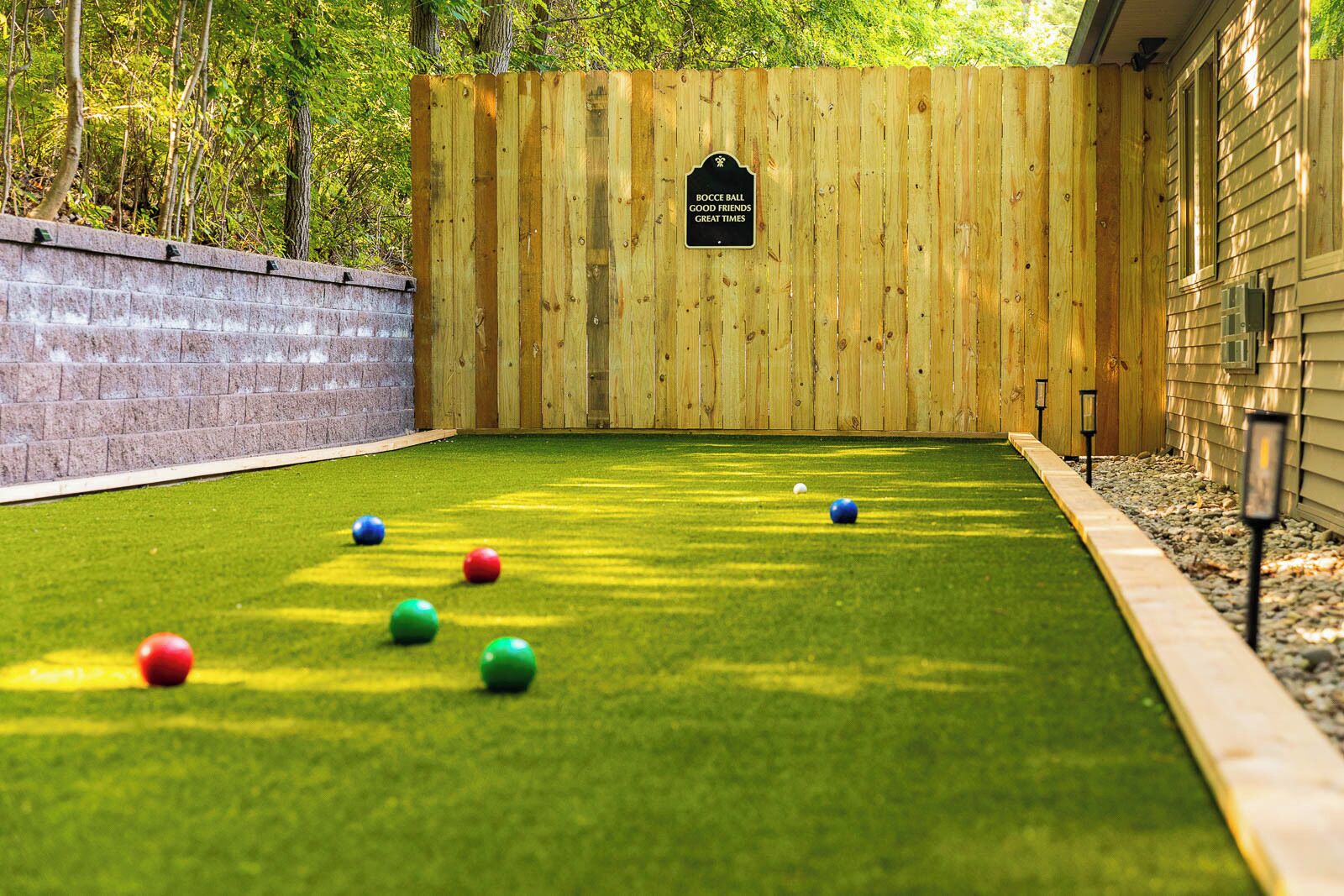 Una cancha de bochas con una cerca de madera, un muro de ladrillo y una zona cubierta de césped.