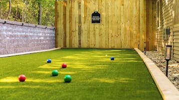 Una cancha de bochas con una cerca de madera, un muro de ladrillo y una zona cubierta de césped.