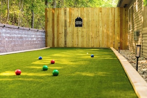 A bocce ball court with a wooden fence, a brick wall, and a grassy area.